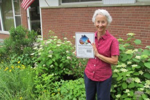 Fran Glass stands in her yard of native plants with a sign proclaiming her Bring Conservation Home Platinum certification - the highest level.