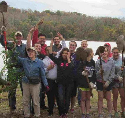 volunteers with hands raised and shovels at a lake