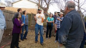 People gathered around a man speaking in a yard
